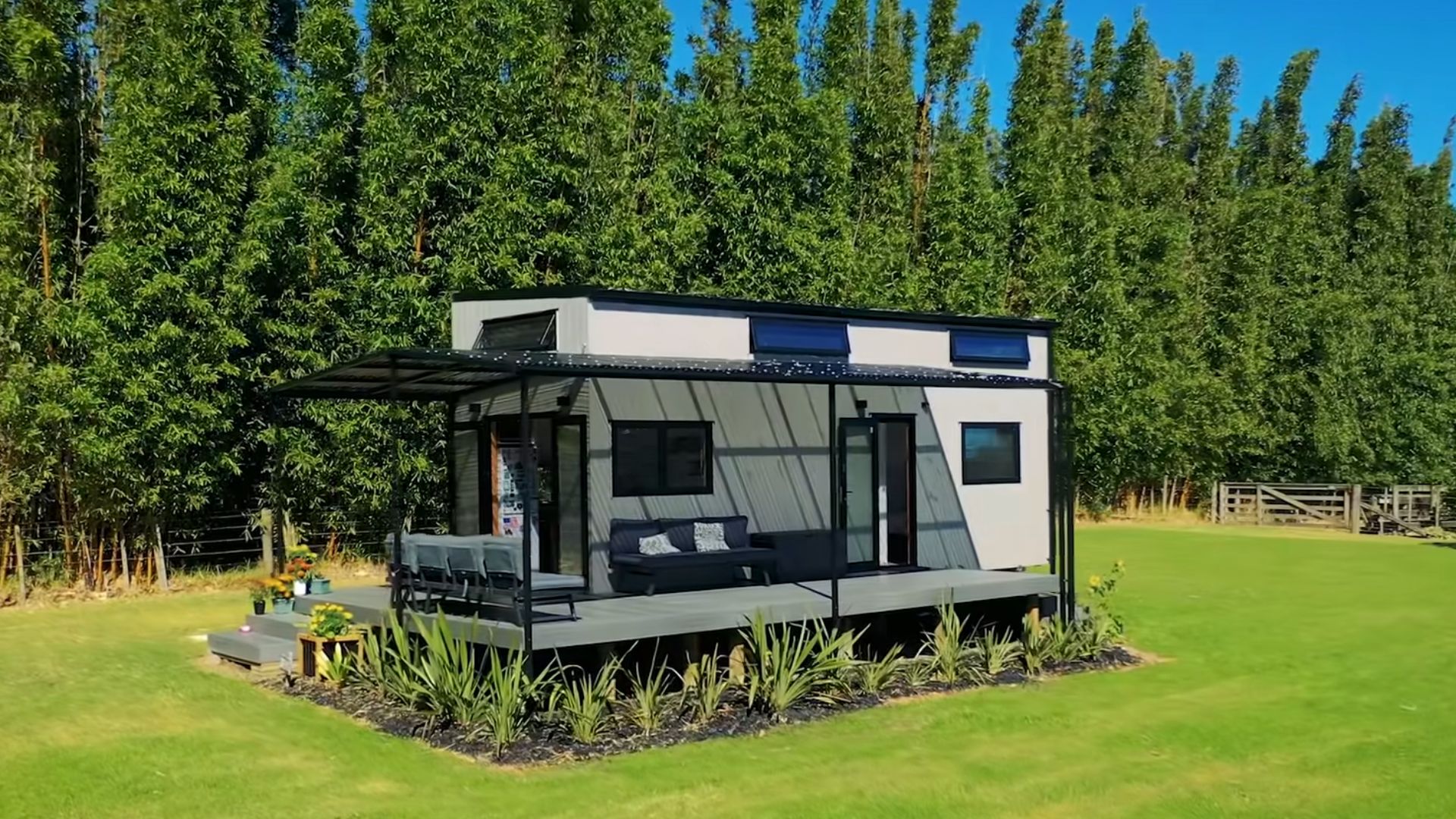 exterior of the tiny house on wheels, with a covered deck and a seating area, surrounded by forest and greenery