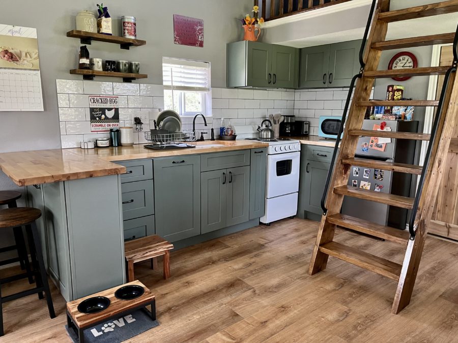 kitchen with green cabinets, brown countertop, brown hanging shelves and ladder that lead into the loft