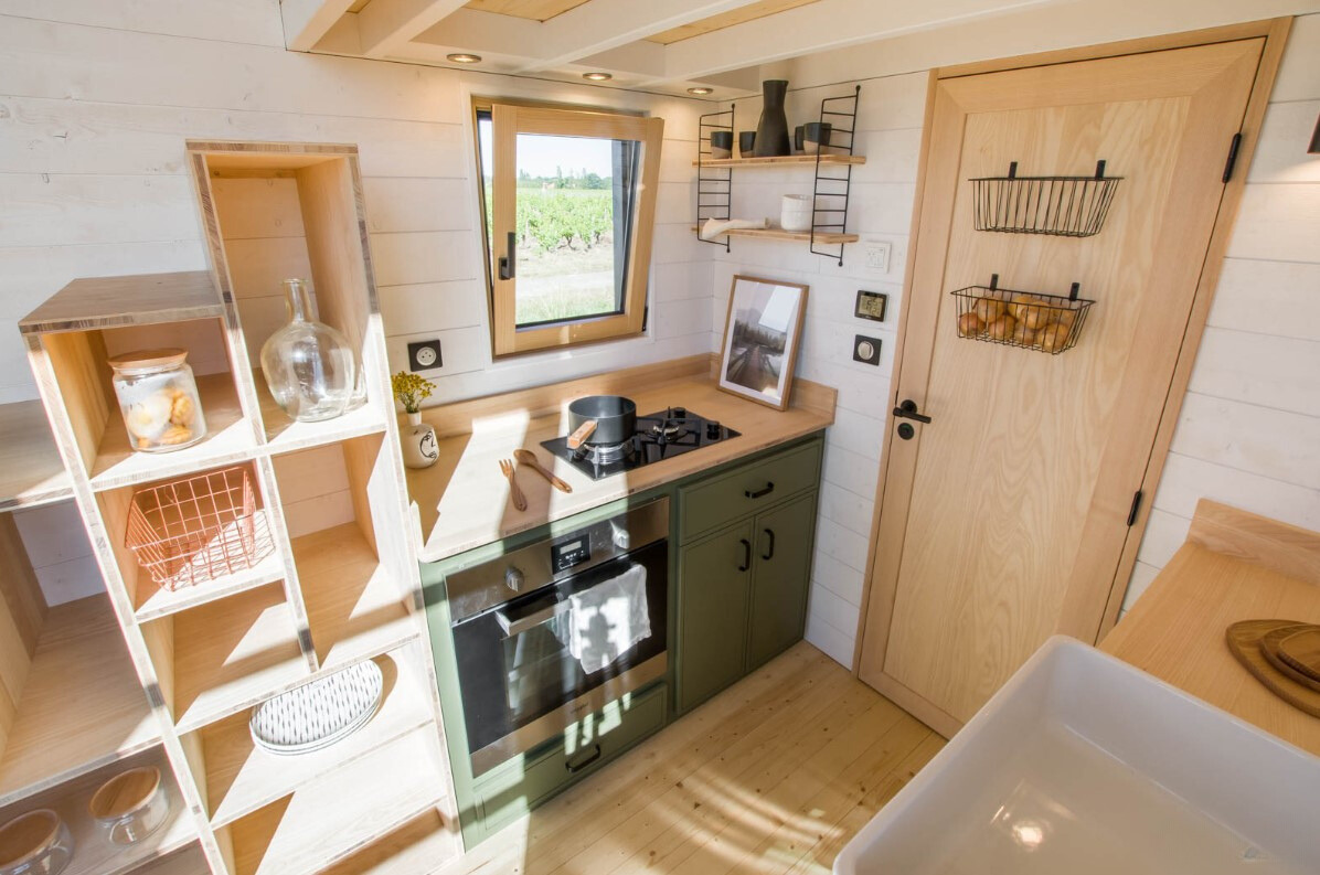 kitchen with green cabinets, window above the stove, stairs with open shelves