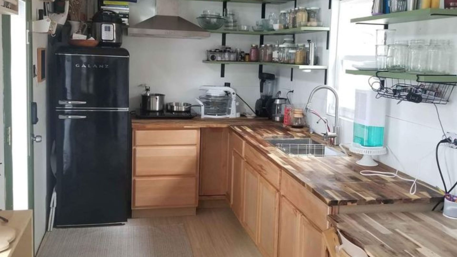 THOW kitchen with a black fridge, open shelves instead of upper cabinets, bottom cabinets in beautiful wood color and butcherblock countertops