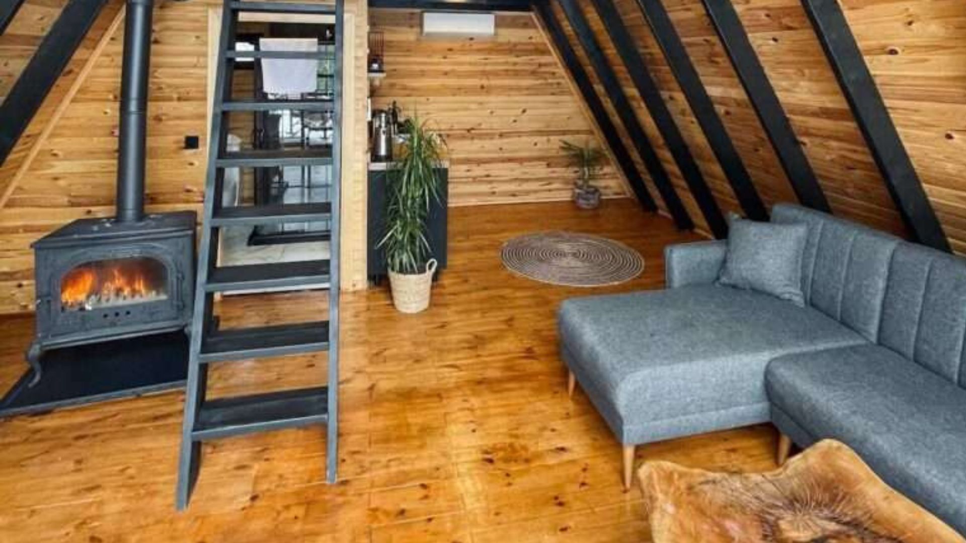 living room with a grey L-shaped sofa, a unique wood table, fireplace on the left right next to the black ladder leading to the loft