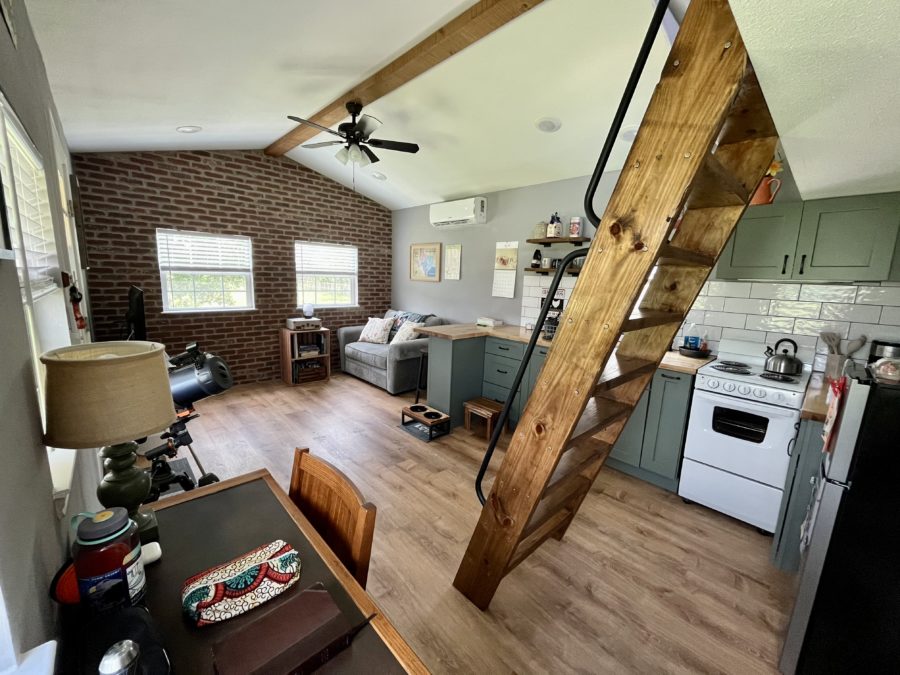 kitchen with green cabinets and brown countertop, living room with a brick wall and gray couch