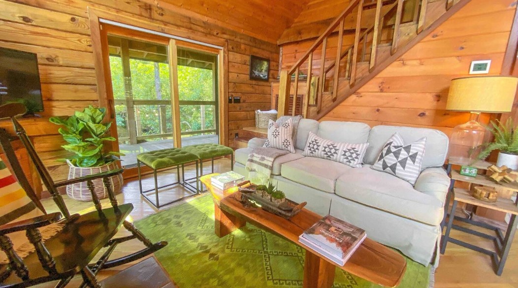 living room with a white couch, wooden wall, green carpet, green cushioned sitting areas, plant, floor to ceiling window and a brown table