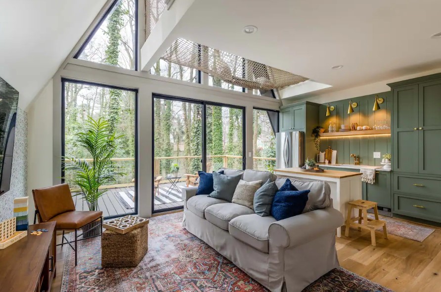 living room with an off-white couch with a flat-screen tv opposite it, floor to ceilings window and a brown leather chair in the corner next to a plant