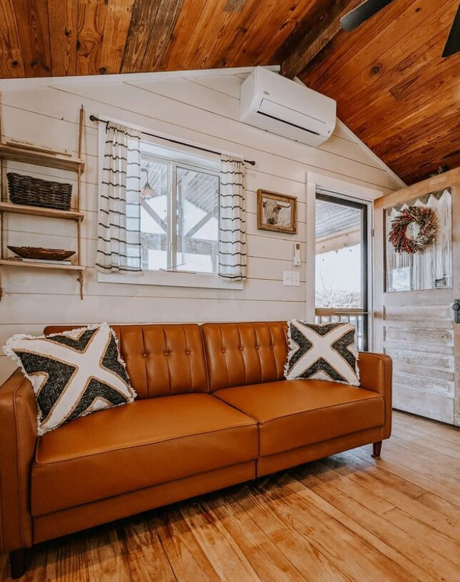 living room with an orangey brown couch and white wooden walls and a brown wooden ceiling and floor