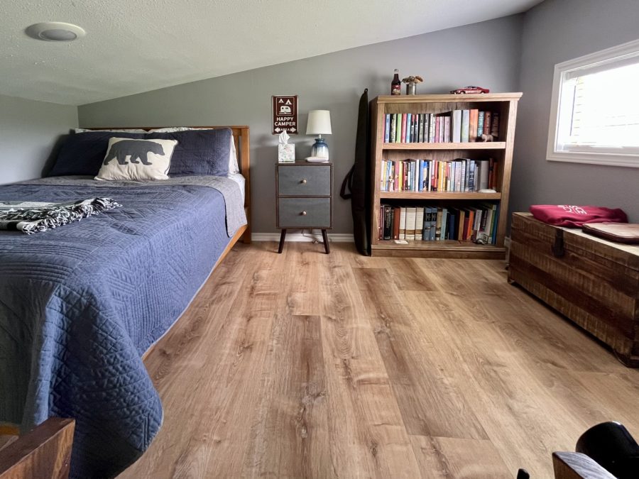 loft bedroom with a bed, brown cabinet with open shelves, bench under the window