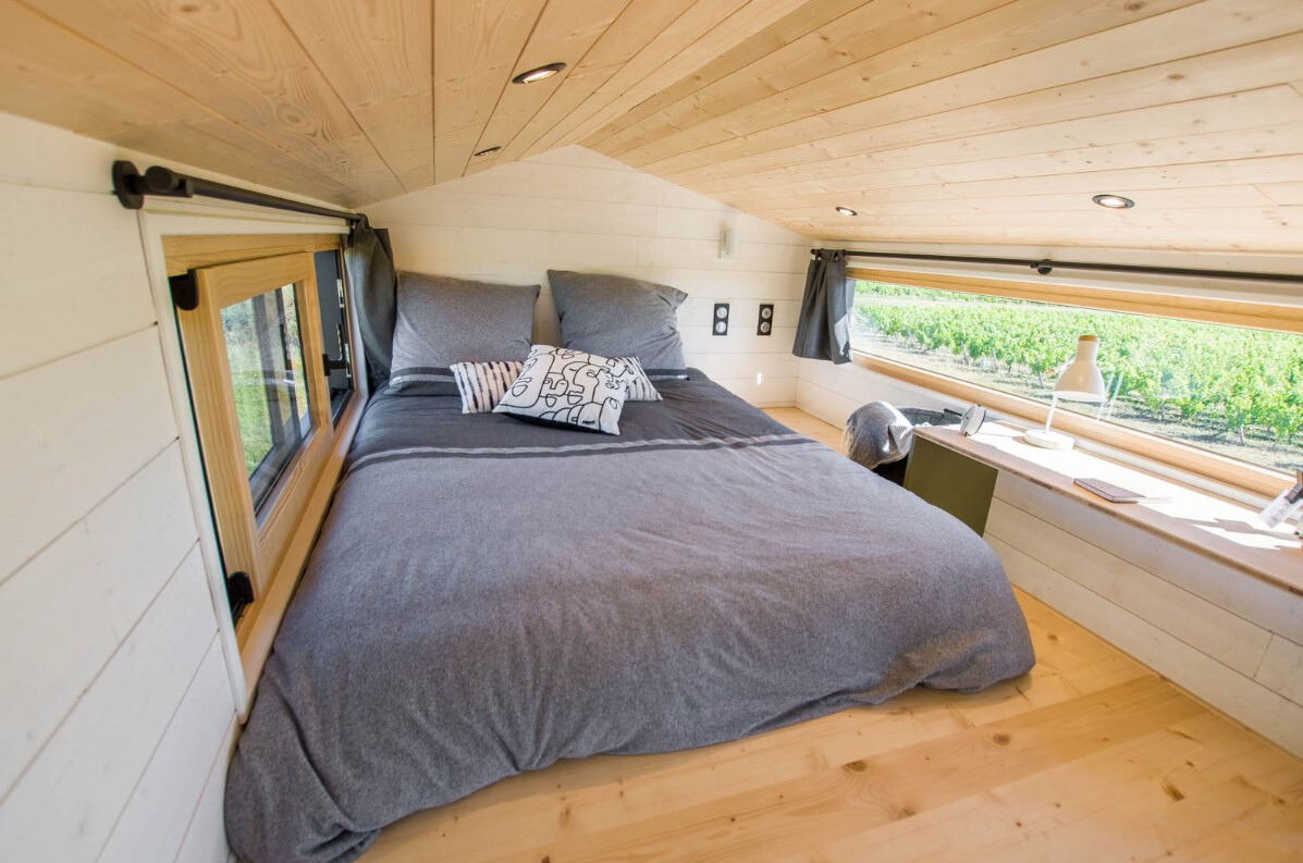 loft bedroom with a big bed, windows on both sides and a brown built-in table