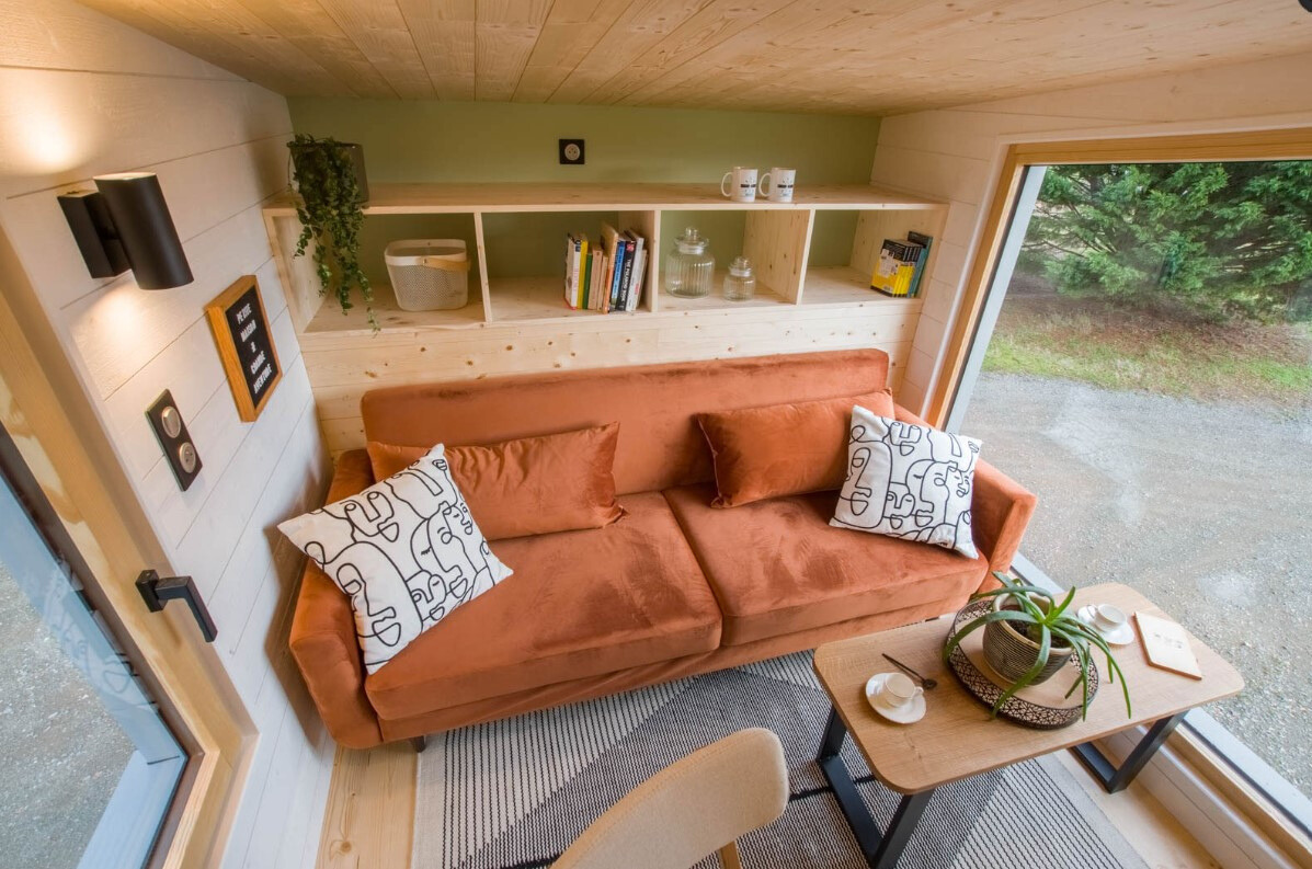 loft living room with an orange couch, two windows and a shelf behind the couch