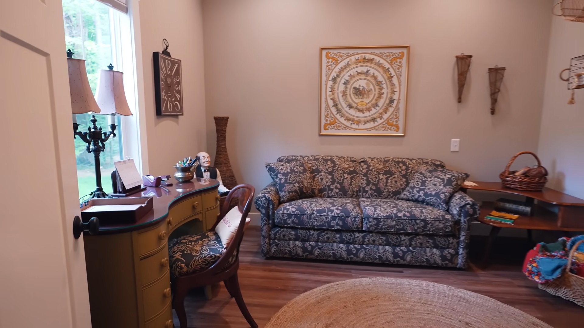 a room with a brown desk, patterned couch and a window above the desk