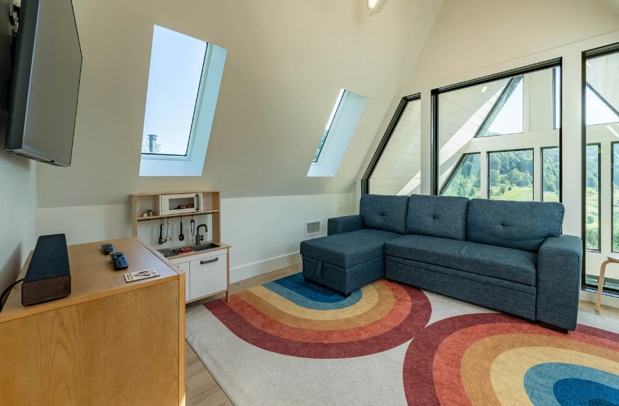 playroom for kids with a colorful carpet with rainbows, mini l-shaped couch, mini kitchen, flat-screen tv and big windows