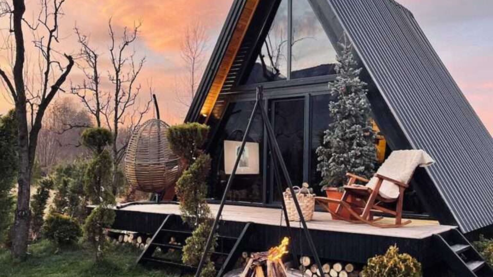 side photo of the A-frame bungalow perla in winter time with a fire pit visible, Christmas tree on the front porch, rocking chairs and some lounge chairs as well