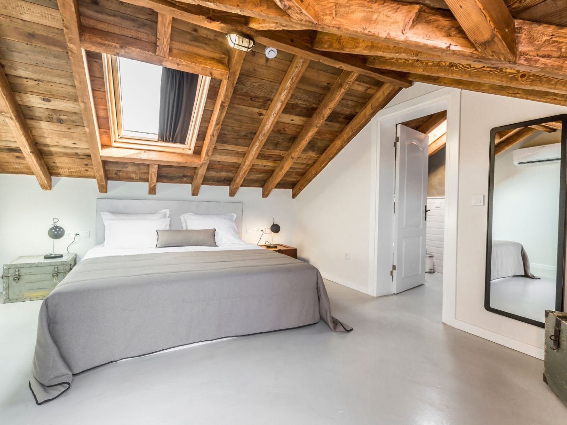 attic bedroom with a wooden ceiling, exposed beams, white walls, an a light grey bed