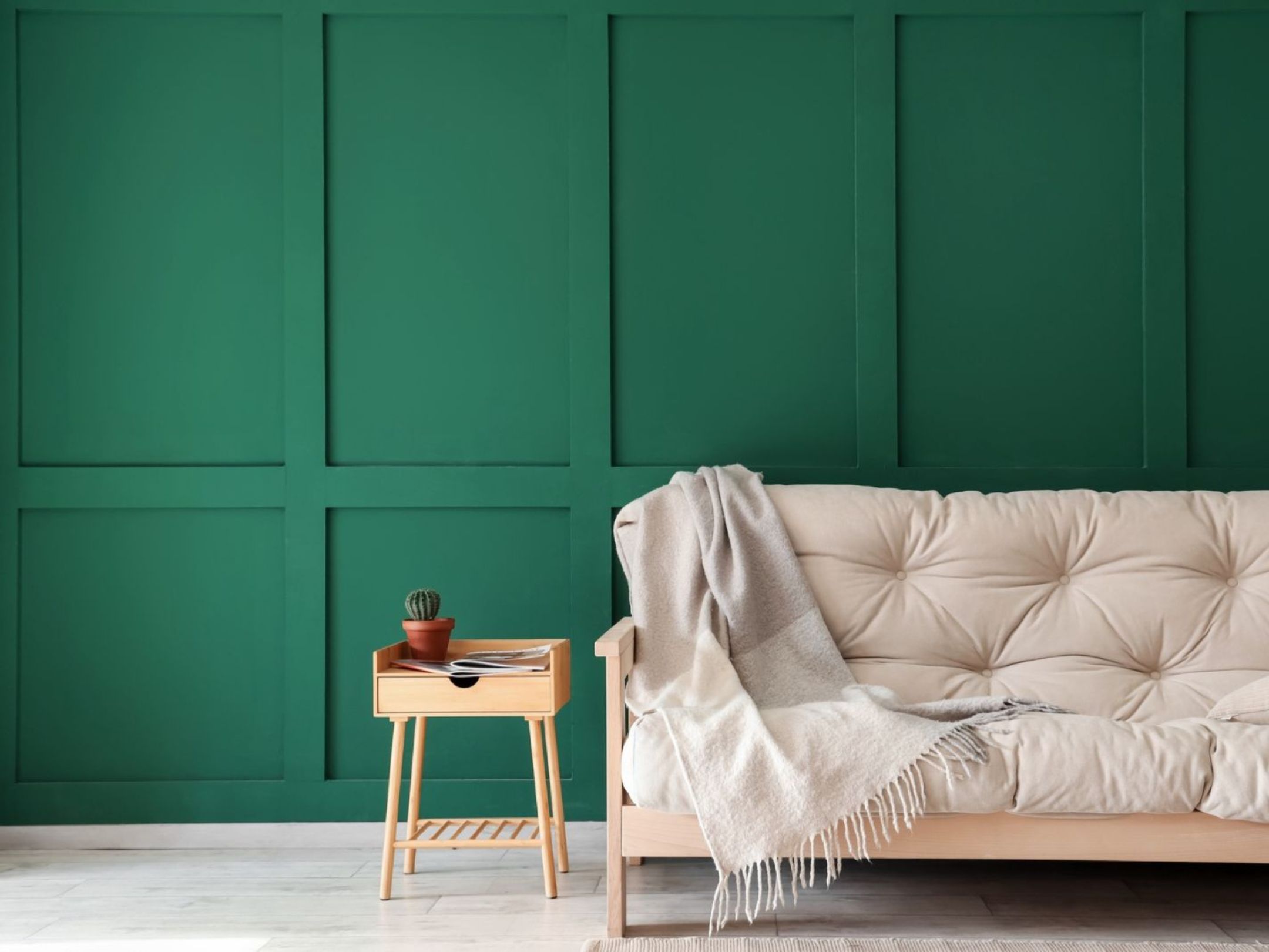 emerald green accent wall, beautiful beige sofa and a small side table with a cactus plant on it