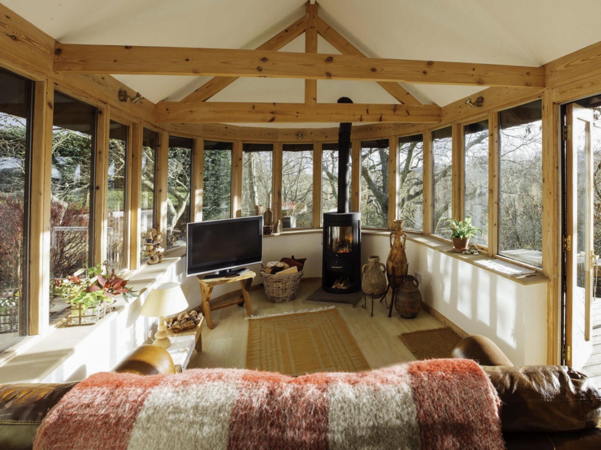 living room with windows all around, flat-screen tv, black fireplace, wood beams, brown carpet