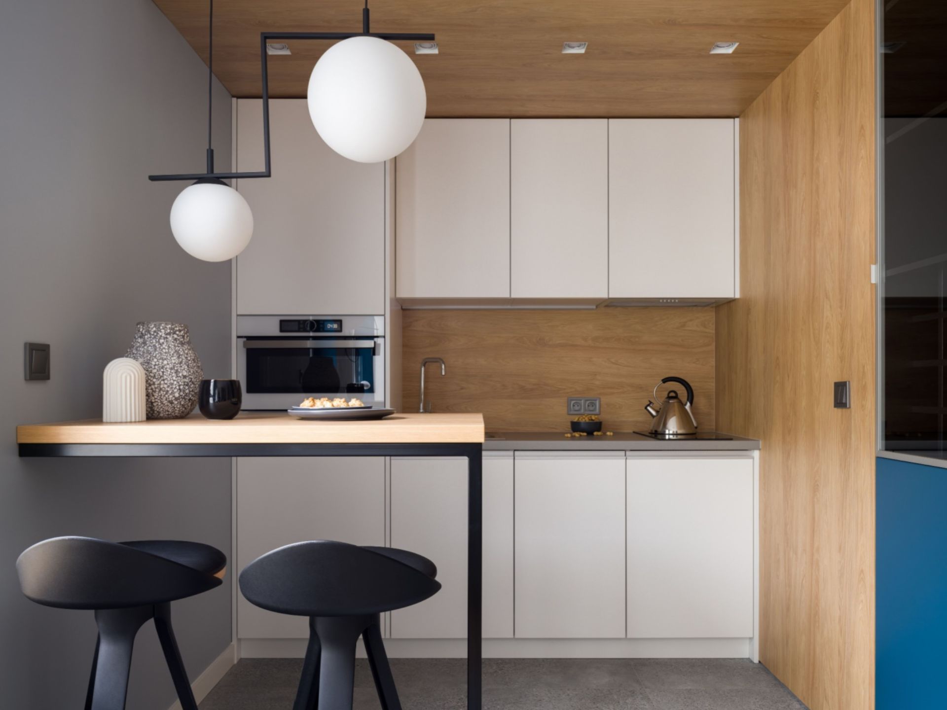 kitchen with white cabinets, wooden walls and one gray wall, built-in table with black bar stools