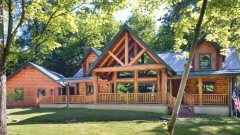 exterior of a log cabin surrounded by greenery and an american flag in front of it