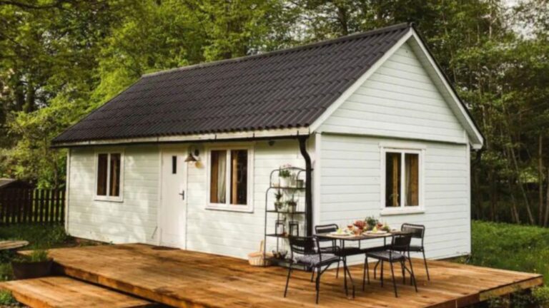 exterior of the small house with a patio, white wood planks facade and a grey, A-frame roof