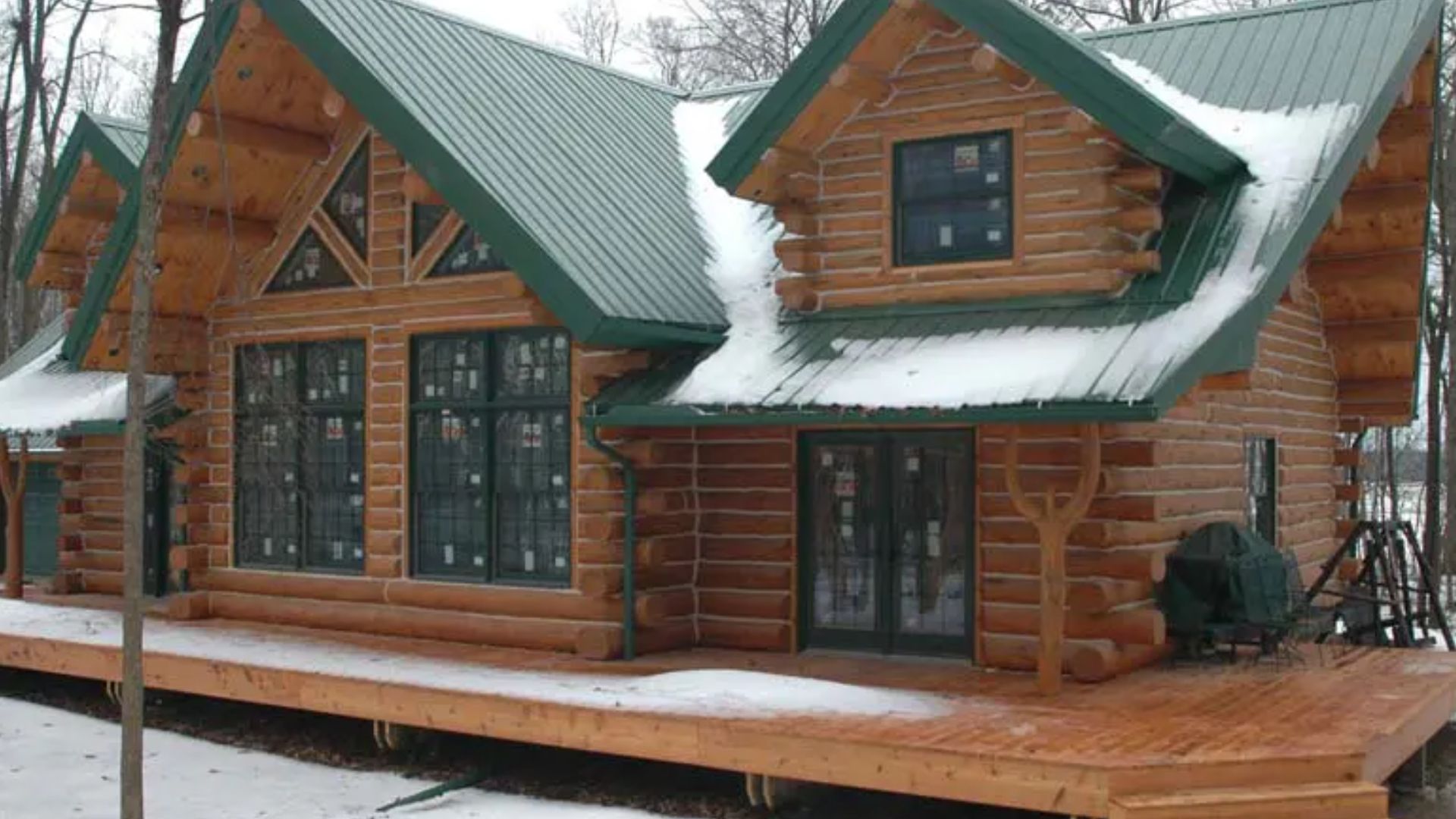 keplar cabin with stained log exterior and green metal roof, double garage adjacent, surrounded by trees