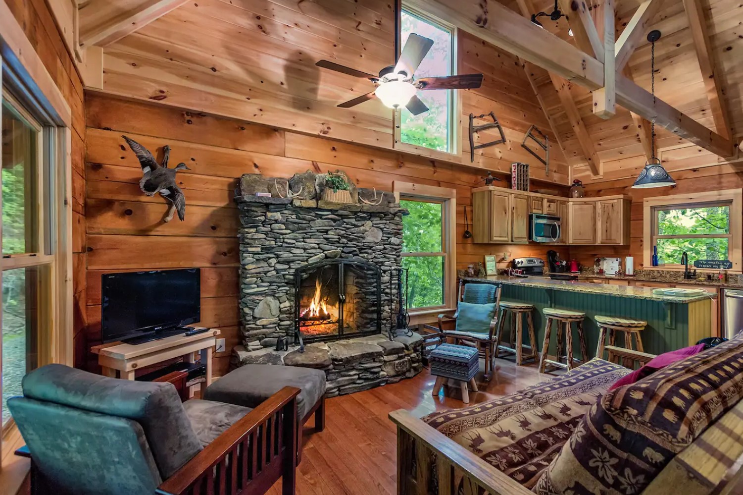 Living room with stanched stone fireplace, comfy couches and chairs and a TV