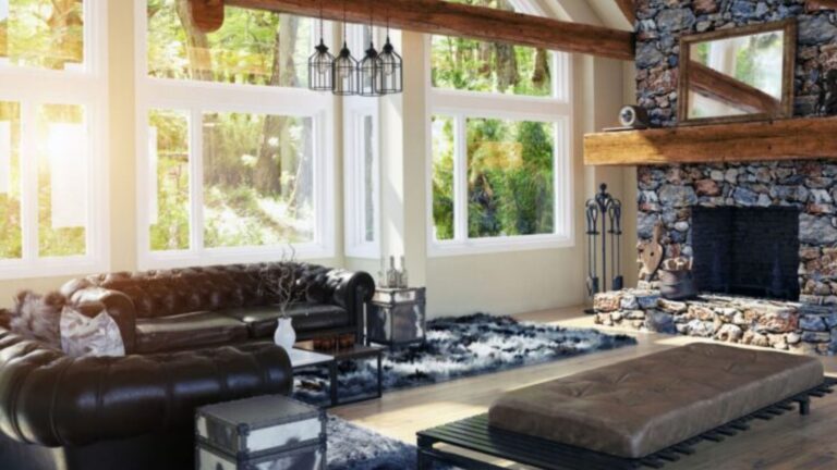 chalet-style living room with black leather furniture, a massive stone fireplace, exposed beams on the ceiling, window wall in the back