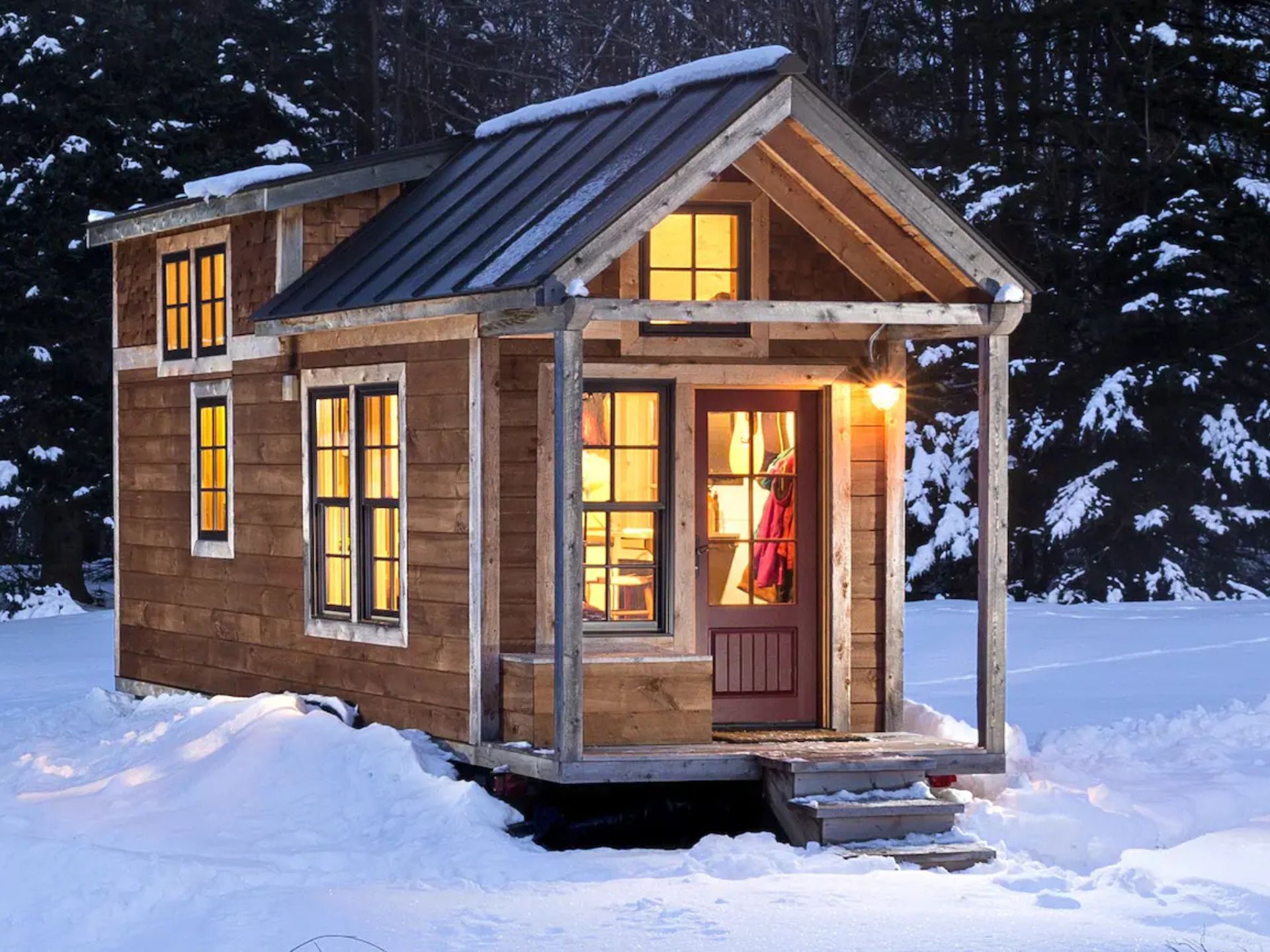 small house with red door covered in snow with lights on