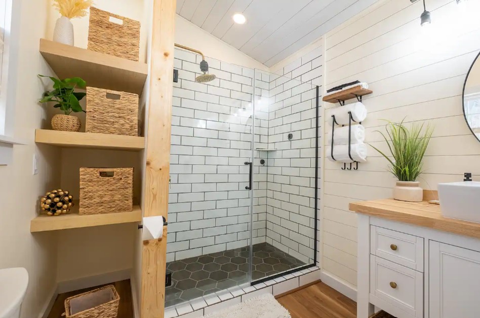 bathroom with a glass shower with black and white tiles, light brown wooden shelves and countertop and a white cabinet