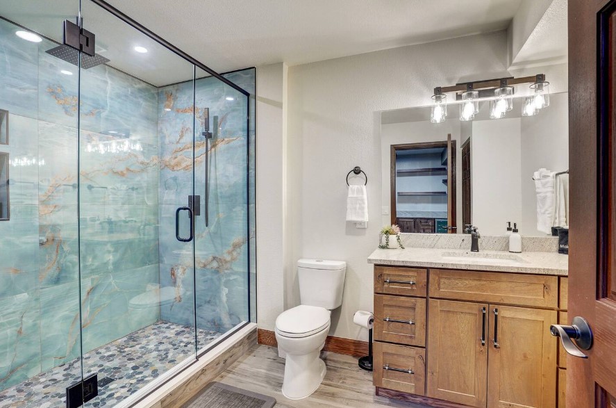 bathroom with blue tiles in the glass shower, brown cabinet and the mirror above it