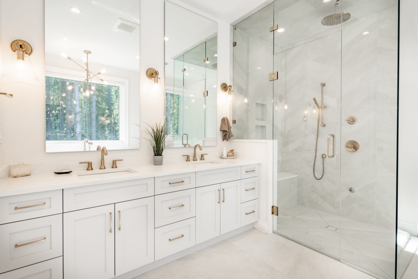 bathroom with a glass shower, white tiles, white cabinets, two mirrors above the sinks with a golden faucet and golden handles