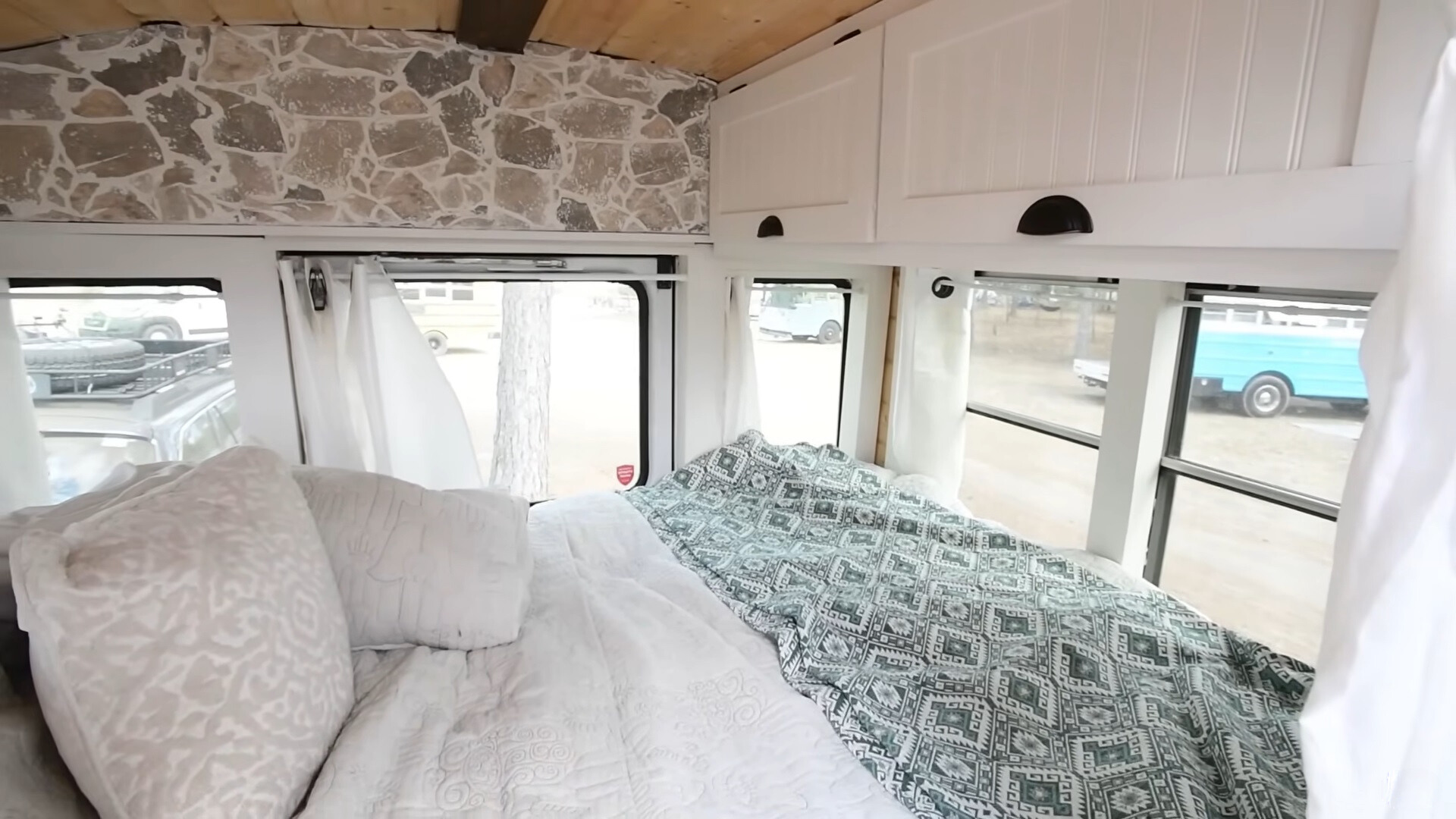 bedroom with a queen-sized bed and windows all around, white cabinets opposite the bed