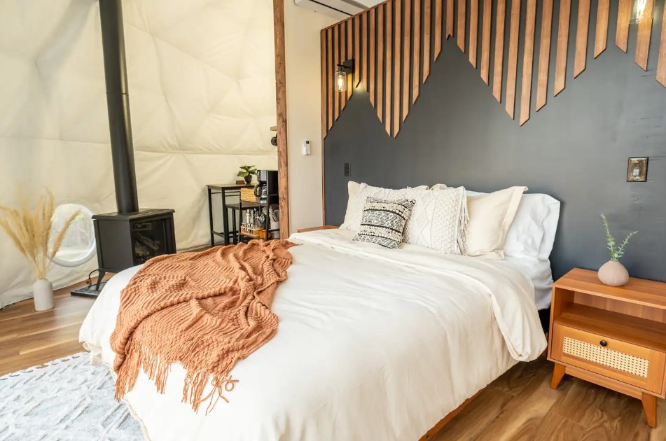 bedroom with a queen-sized bed, small black fireplace and a brown bedside table