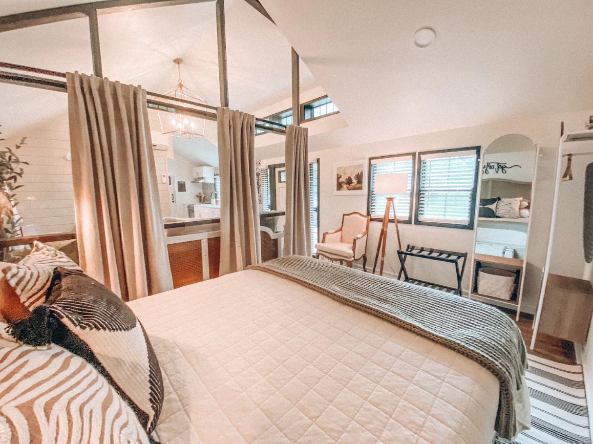 bedroom with a queen-sized bed, curtains serving as a divider from a living room, tall mirror with an arched top and a tall lamp