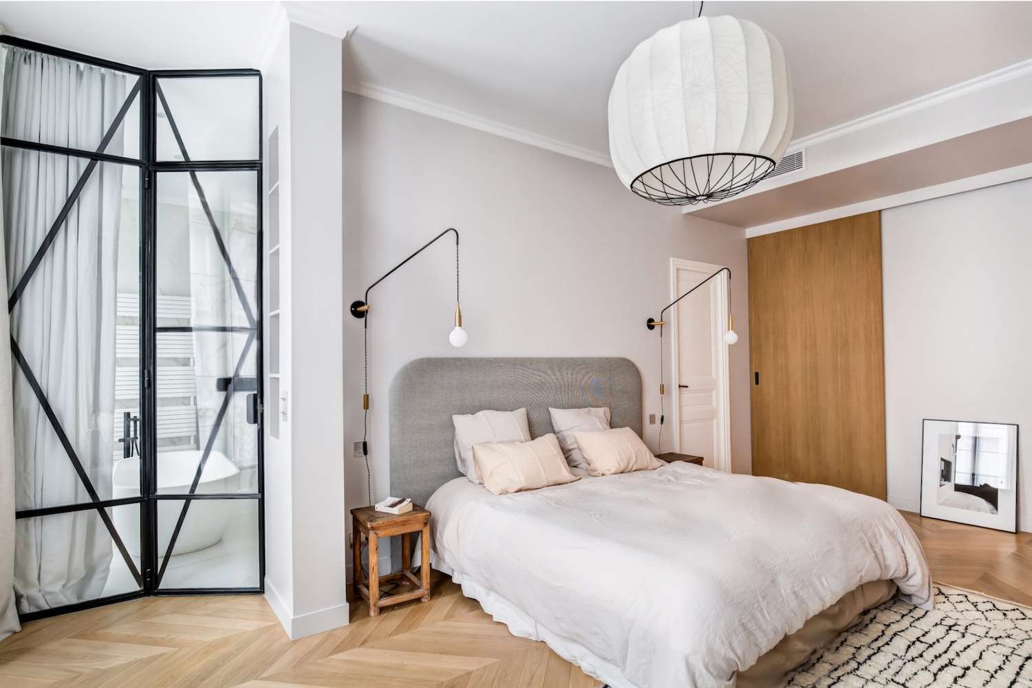 bedroom with a comfortable bed, brown tiny bedside table, white chandelier above the bed, gray headboard and white walls