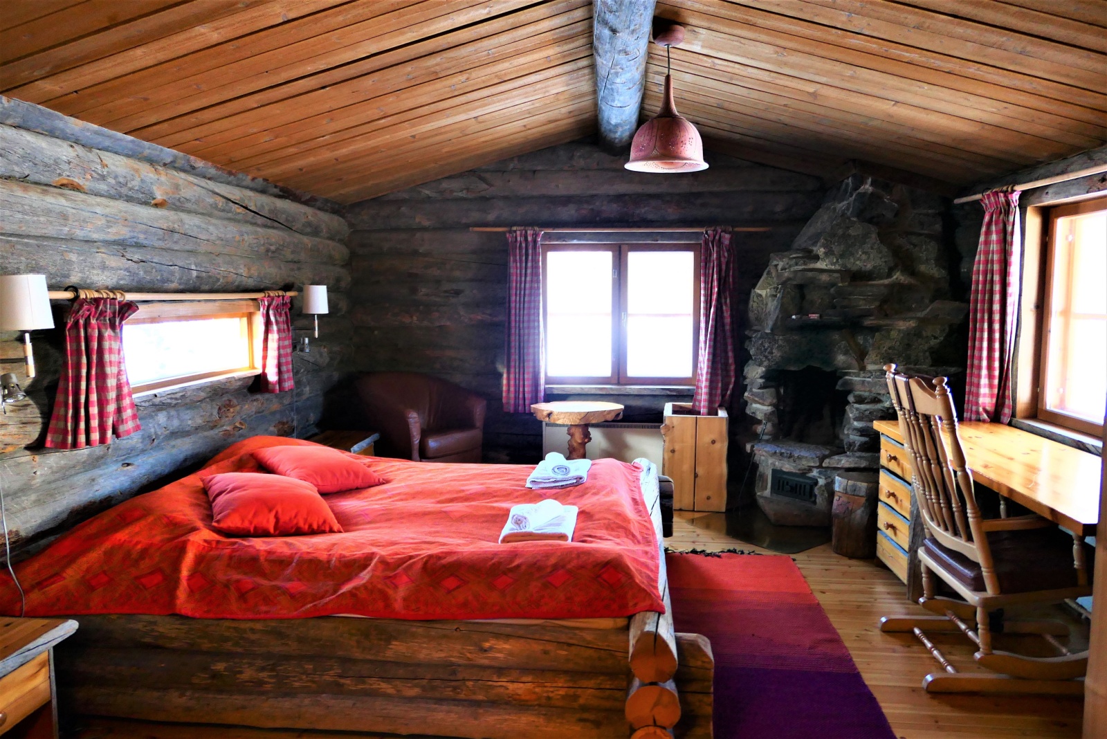 bedroom with wooden walls, brown, wooden desk opposite the bed with a wooden bed frame, wooden chair next to the bed