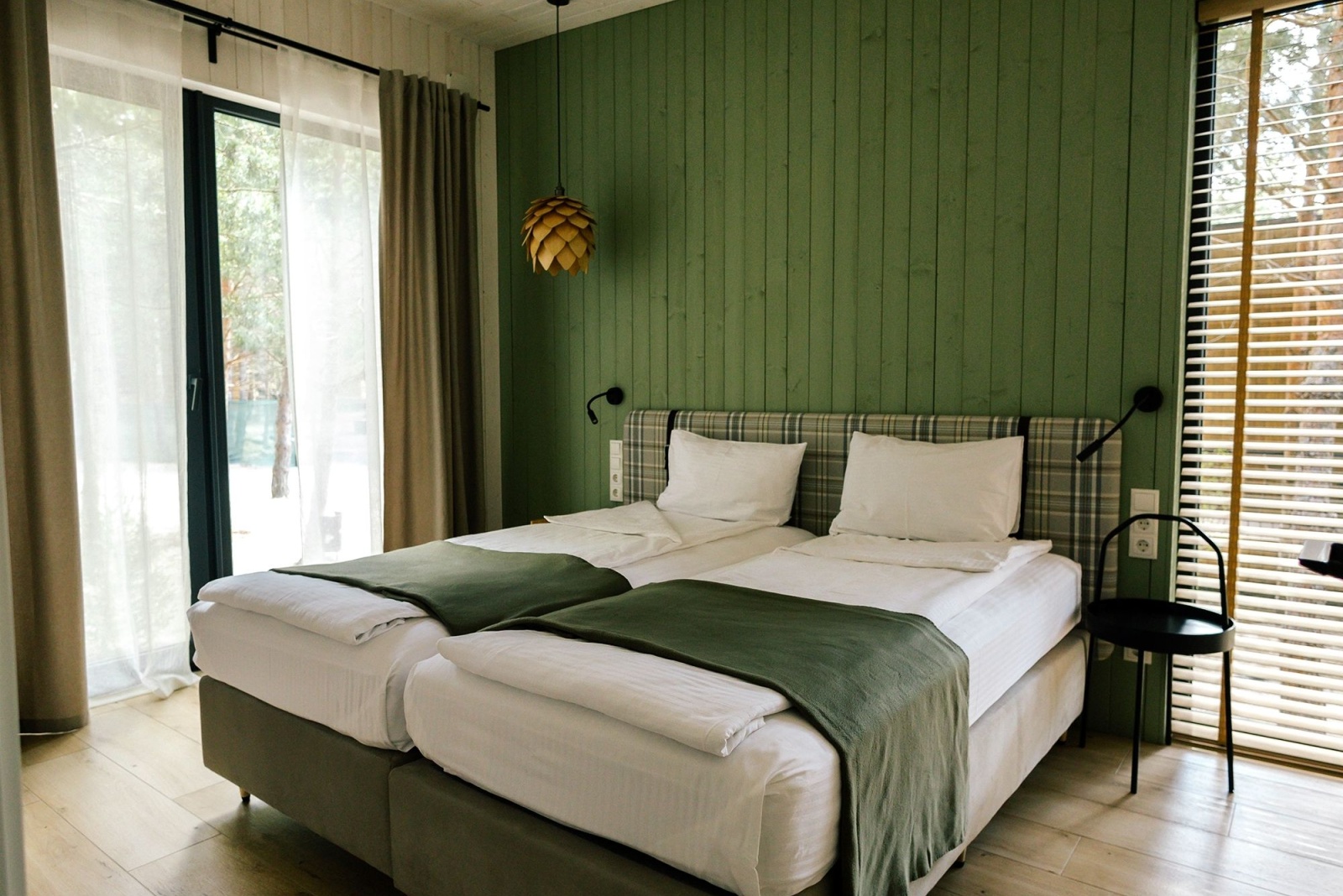 bedroom with a wooden green wall, floor to ceiling windows and green and white sheets