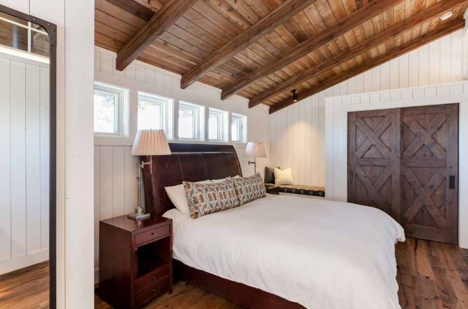 bedroom with a wooden wall, wooden ceiling with wooden beams, barn door, brown bed frame, brown wooden bedside table