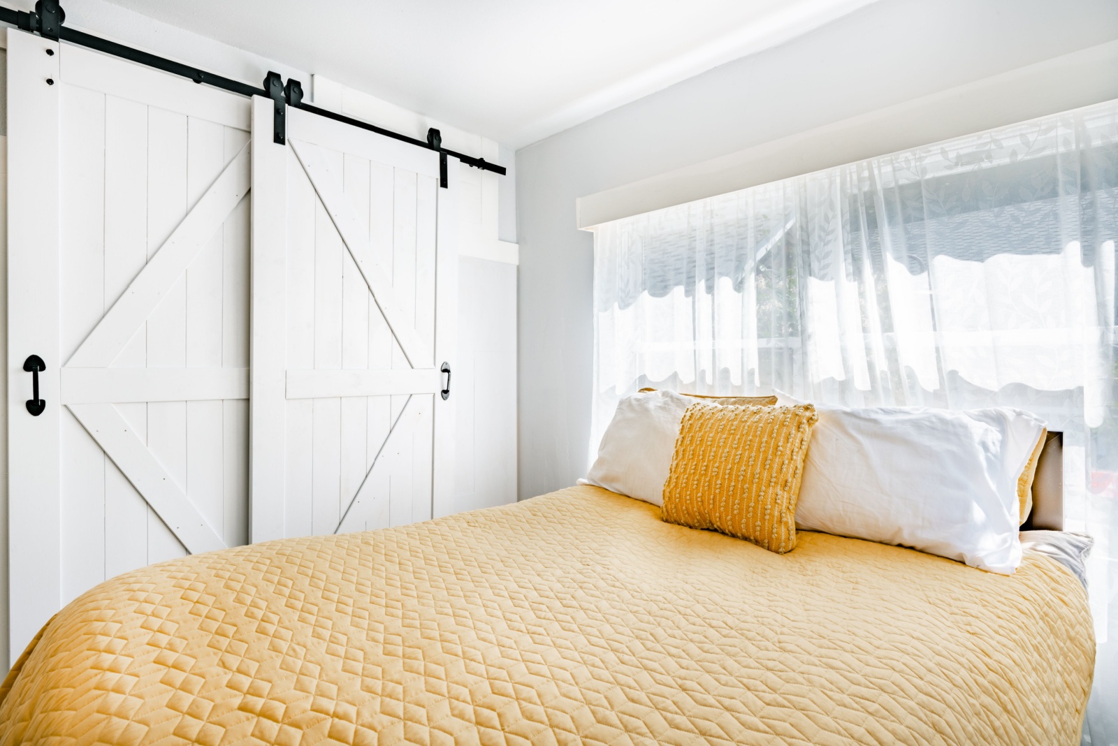 bedroom with white barn doors, window above the bed, yellow bed sheets