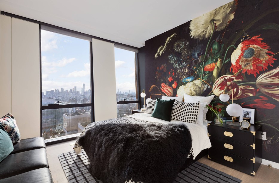 bedroom with one floral patterned wall, floor to ceiling windows, a bed, brown cabinet next to the bed