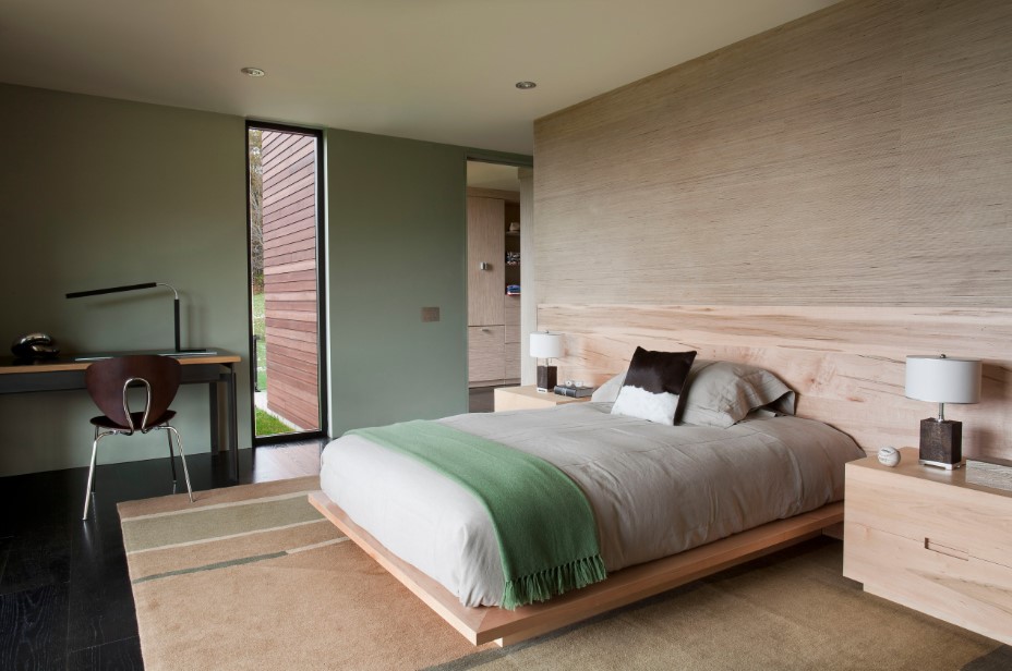 bedroom with one green wall, one wooden wall, a bed with a wooden headboard, wooden cabinet and a desk accompanied by a brown chair