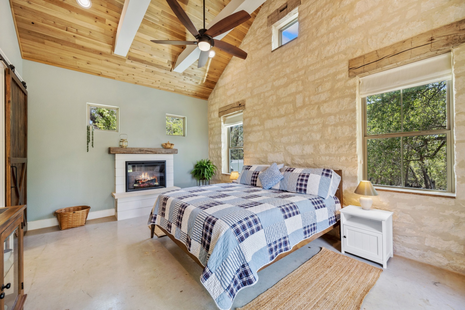 bedroom with a beige stone wall, wooden ceiling and a ventilator, white bedside tables