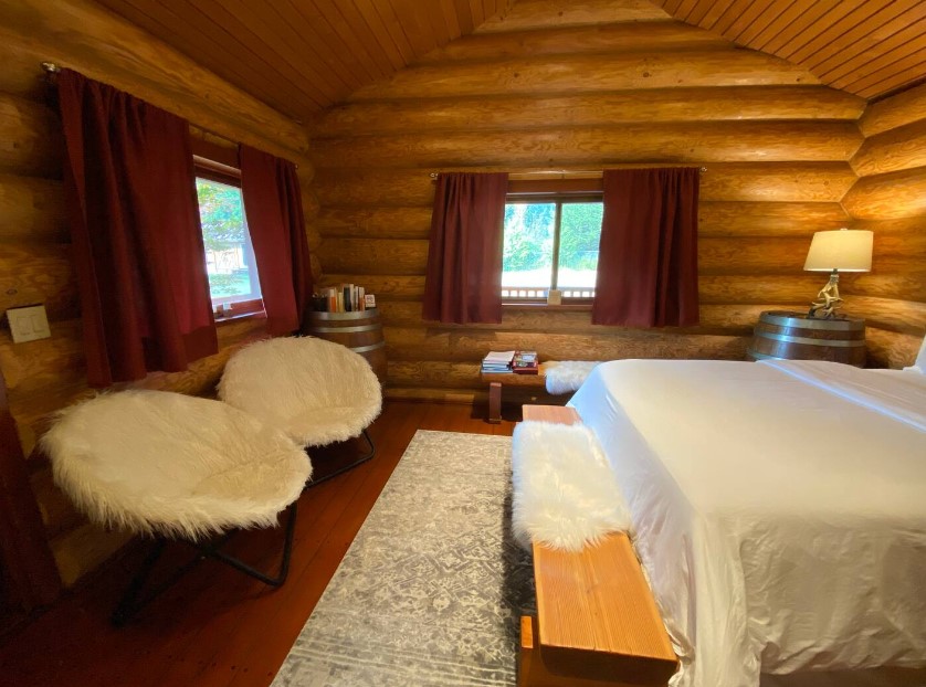 bedroom with two round chairs and a bench with fur cover below the two windows