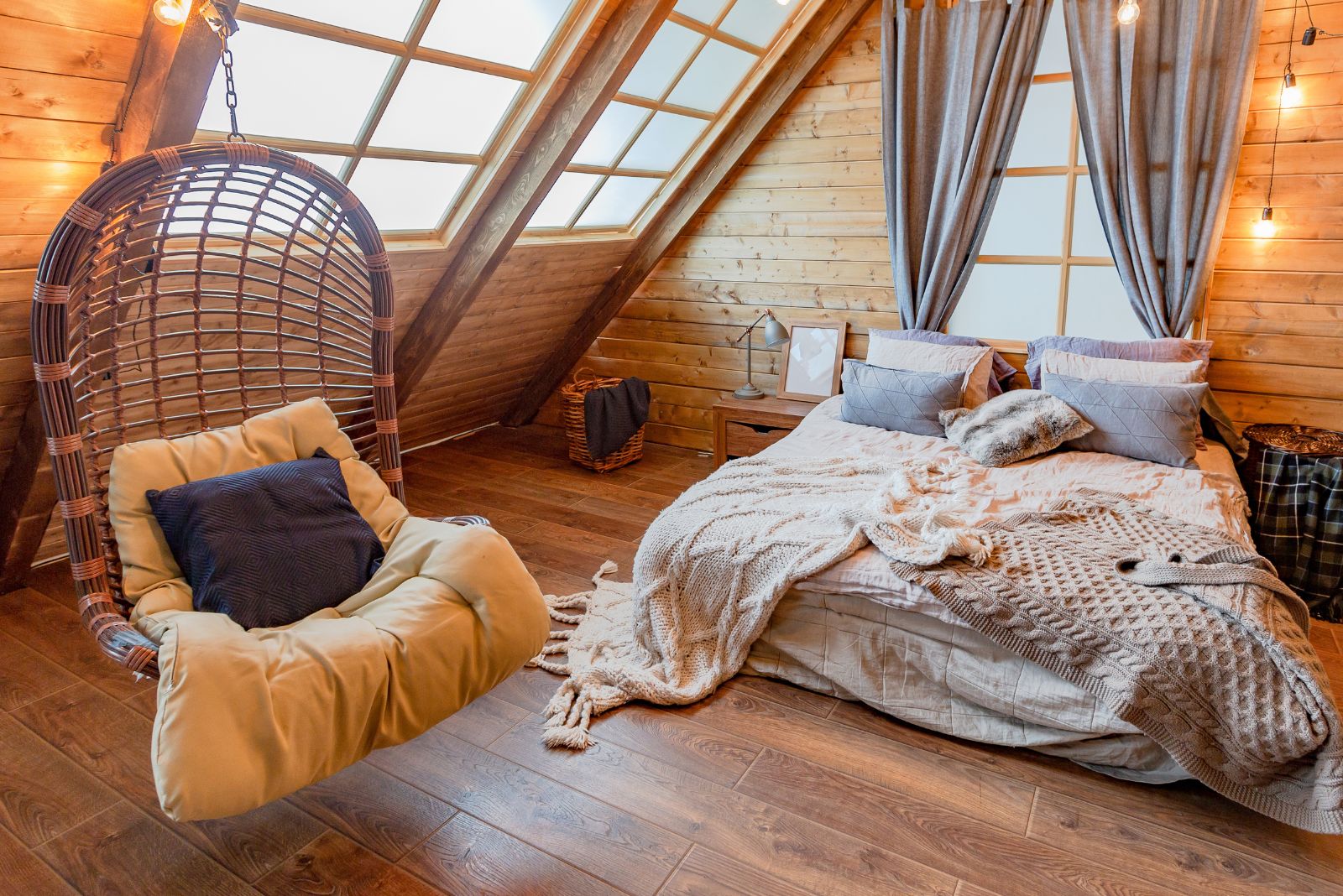 rustic bedroom with a comfy floor bed, grey curtains on the window behind the bed, a cool swing chair on the left