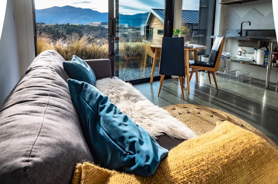 couch of the living room, in the background are dining table accompanied by chairs and floor to ceiling windows