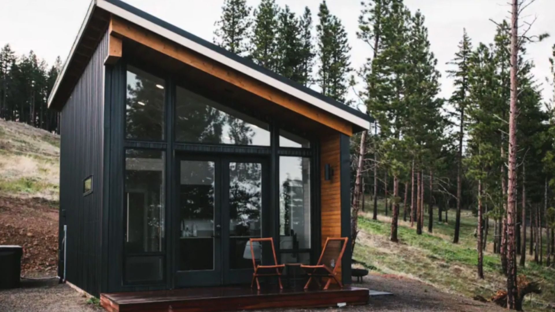 exterior of the cabin with the entrance all in windows, a small deck at the entrance, slanted roof, surrounded with trees