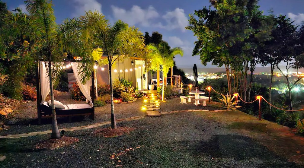 exterior of a container home with an ocean view, canopy bed covered in string lights outside the home