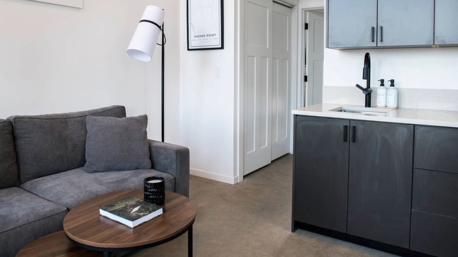 a bit of living roomm sofa in grey visible, a small coffee table in wood color, grey kitchen on the right