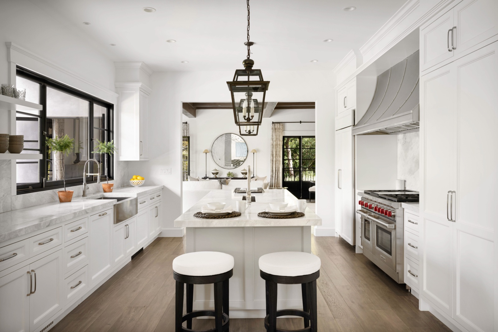 kitchen with a white island in the middle accompanied by black and white chairs, white cabinets and white countertop around the island