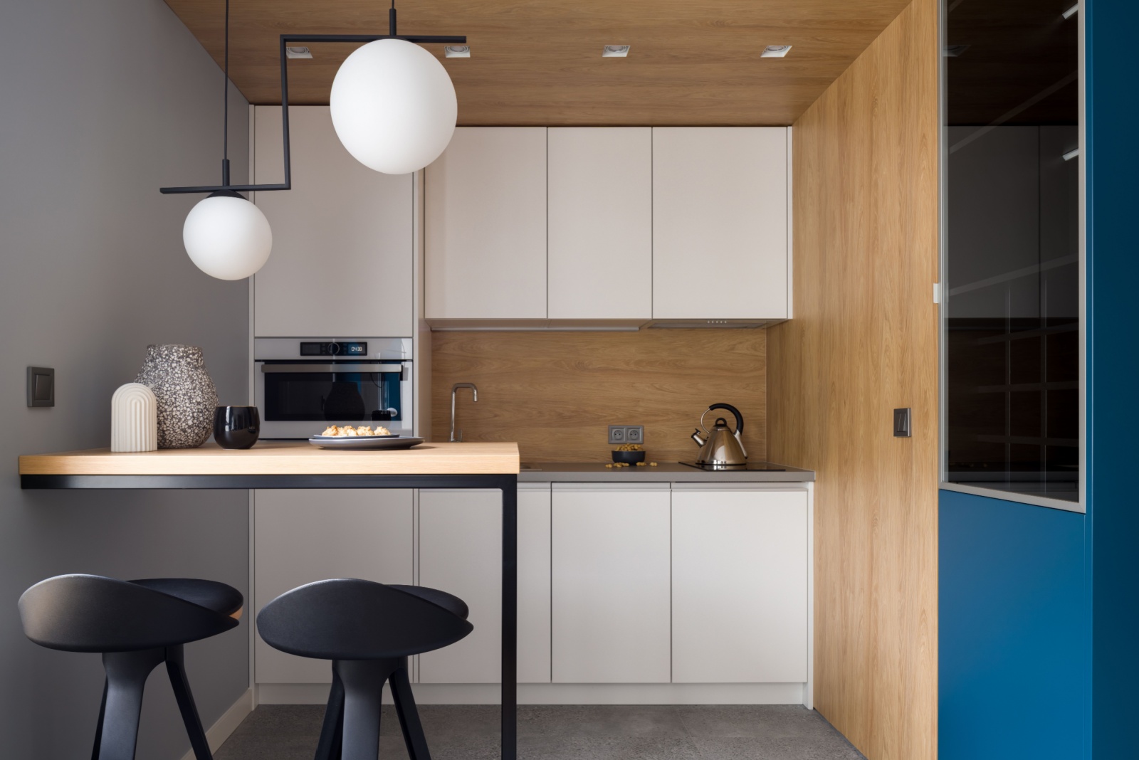 kitchen with white cabinets, wooden walls and one gray wall, built-in table with black bar stools