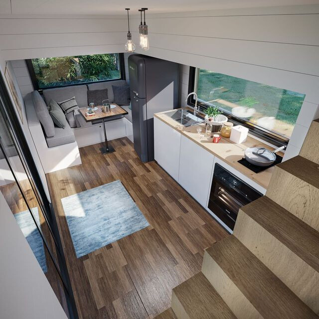 layout of an open space living and cooking area with a wooden countertop, white cabinets, u-shaped built-in gray couch and windows around the entire place