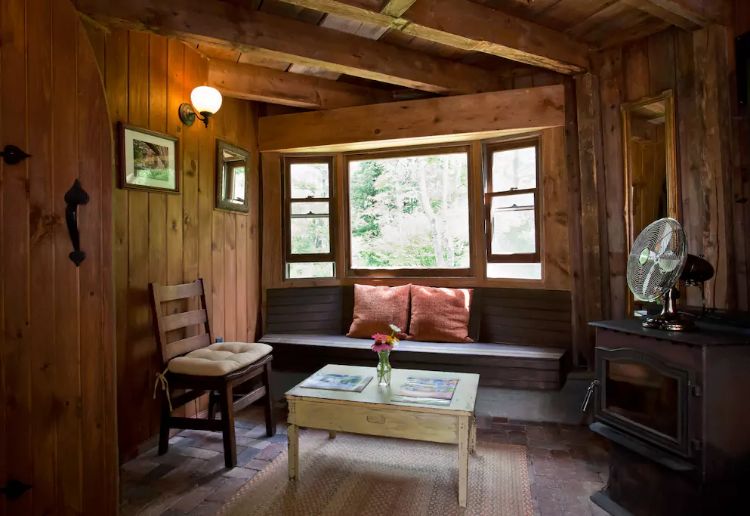 living area of a cabin with a built-in sitting area, a wooden chair, light wooden table and a window above the sitting spot