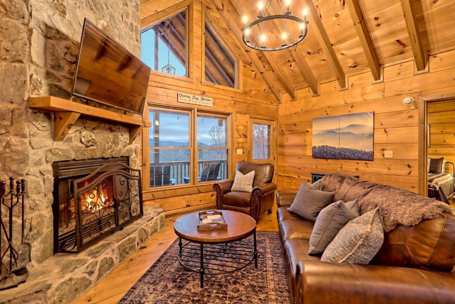 living room with a brown leather couch, big windows, flat screen tv, brown round table and a fireplace